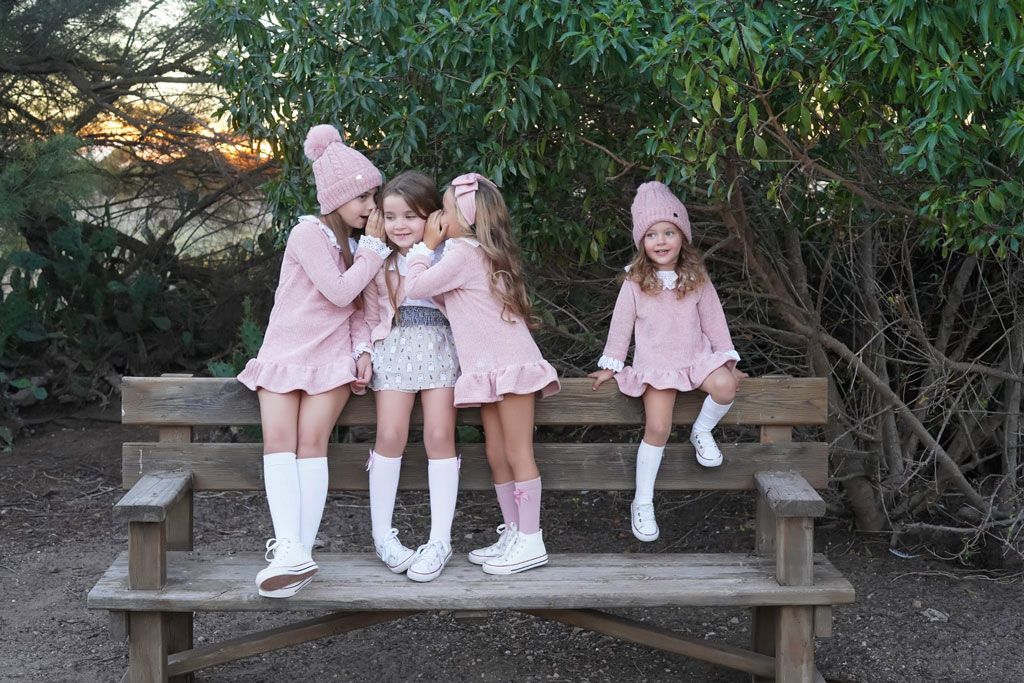 ropa infantil premium con cuatro niñas vestidas con vestido rosas sentadas en banco de madera